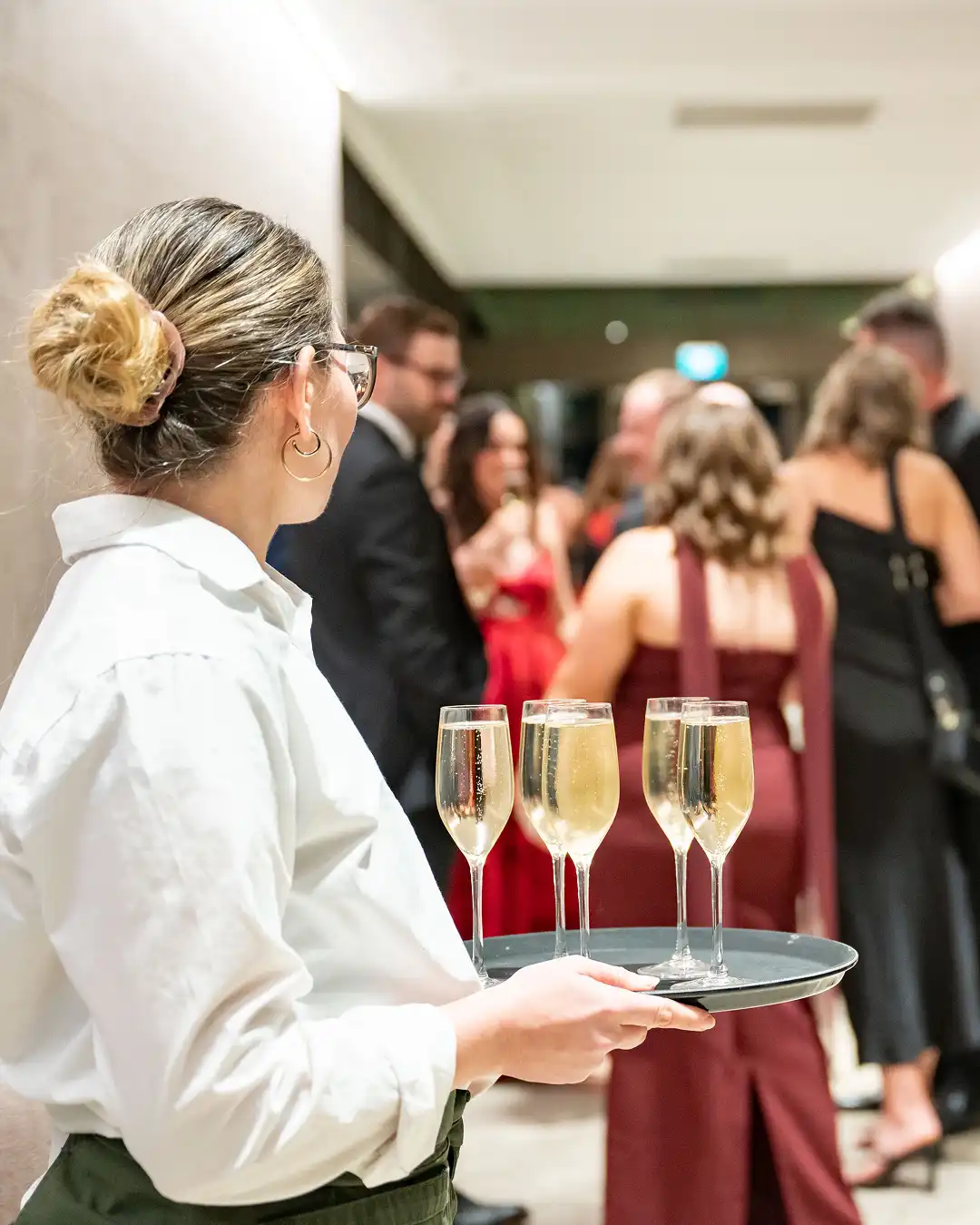 Waitstaff carrying champagne glasses at indoor wedding or event reception